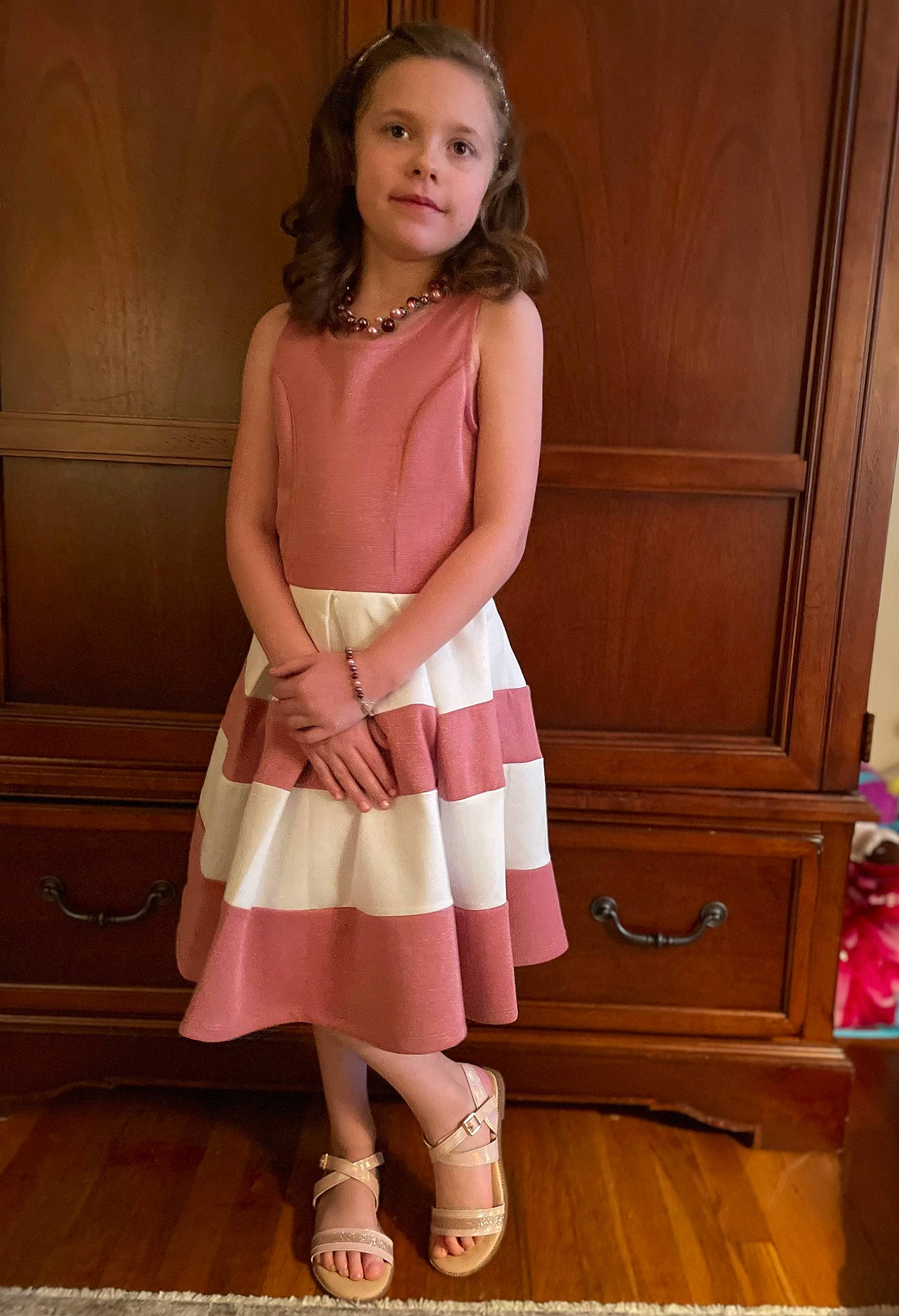 Piper is registered to the contest to win money with this photo: brown_hair, cabinetry, chest_of_drawers, day_dress, drawer, fashion_design, floor, flooring, formal_wear, hardwood, human_leg, knee, magenta, pattern, peach, person, pink, sleeve, thigh, waist