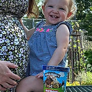 Azona is registered to the contest to win money with this photo: toddler, child, pregnant_woman, ice_cream, ben_and_jerrys, outdoor, picnic_table, smiling, striped_dress, floral_dress, garden, sunlight, happy, person, food_container, blue_sky, fence, hand, nature, cute