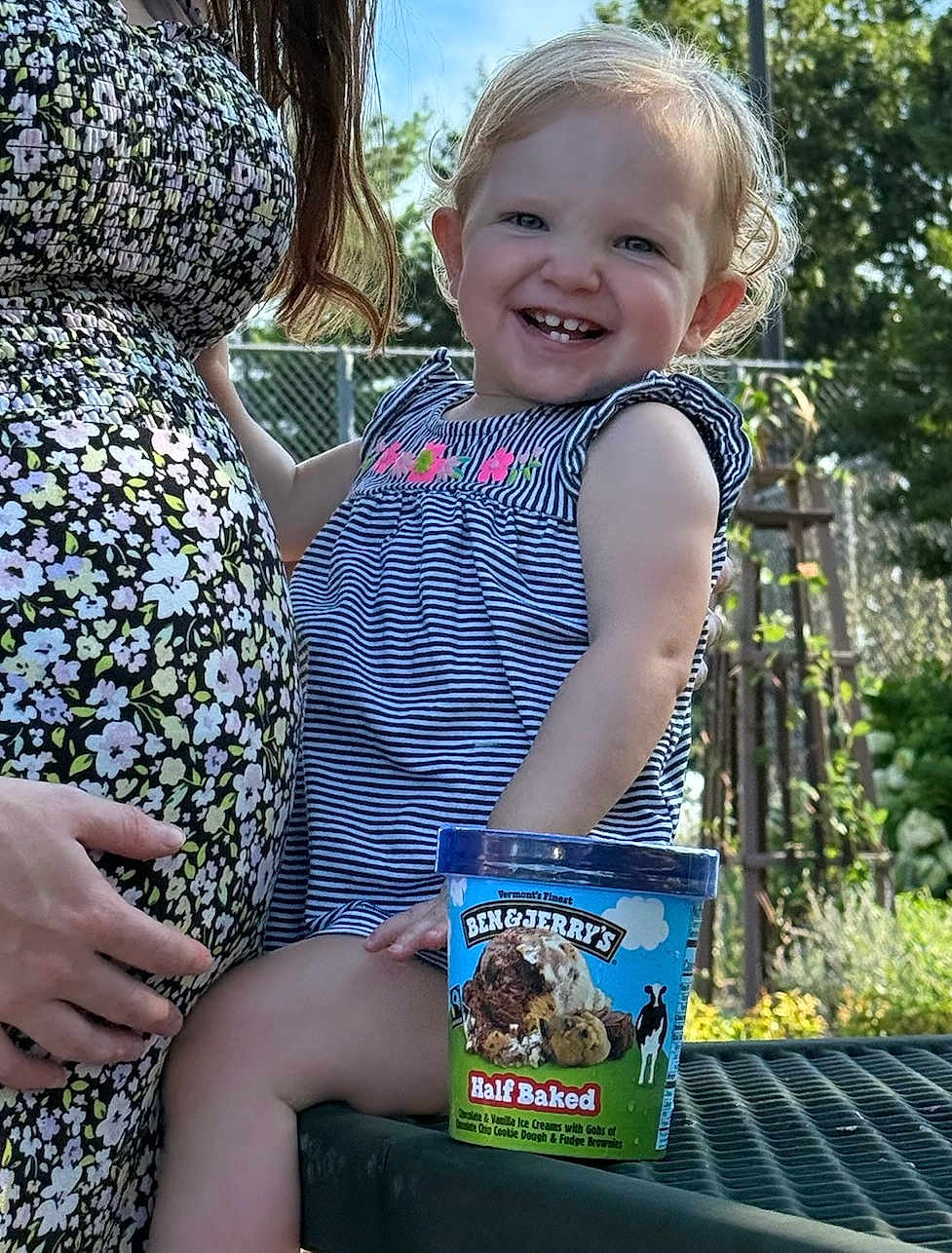 Azona is registered to the contest to win money with this photo: toddler, child, pregnant_woman, ice_cream, ben_and_jerrys, outdoor, picnic_table, smiling, striped_dress, floral_dress, garden, sunlight, happy, person, food_container, blue_sky, fence, hand, nature, cute