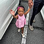 toddler, child, pink_dress, headband, smiling, holding_hand, adult, parking_lot, car, asphalt, white_shoes, road_marking, outdoor, happy, person, casual_clothing, walking, cute, daylight, curly_hair