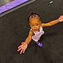 toddler, child, braided_hair, purple_socks, pink_dress, trampoline, floor, reaching, looking_up, indoor, play_area, footwear, person, curly_hair, black_hair, cute, expression, young_child, activity, colorful