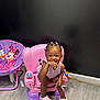 toddler, child, pink_chair, keys, hair_clips, crocs, playful, indoor, floor, black_wall, toy, minnie_mouse_chair, colorful, smile, person, furniture, seated, wooden_floor, cute, small_chair