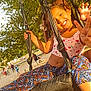 child, swing, tire_swing, playground, smiling, peace_sign, sunlight, tree, park, outdoor, happy, play, summer, sand, rope, clothing, person, fun, nature, leaves