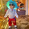 child, costume, hat, sunglasses, indoor, floor, clothing, person, standing, shoes, red_pants, white_shirt, colorful, playful, casual, young_child, portrait, toy_room, light, shadow