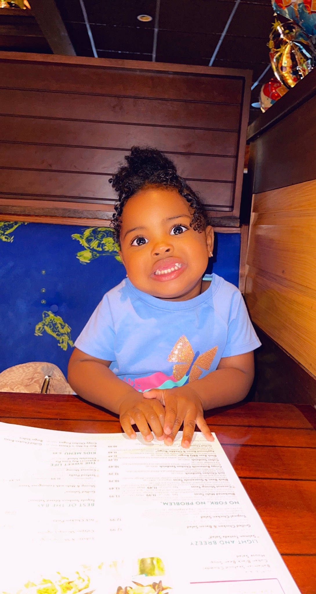 Aubriella is registered to the contest to win money with this photo: afro, child, electric_blue, flooring, font, fun, happy, hardwood, joy, person, room, sitting, smile, t_shirt, thumb, toddler, varnish, wood, wood_stain