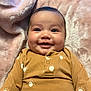 baby, smiling, infant, face, eyes, blanket, brown_clothing, patterned_clothing, happy, cute, portrait, indoor, soft_texture, cozy, child, young, person, head, skin, eyebrows