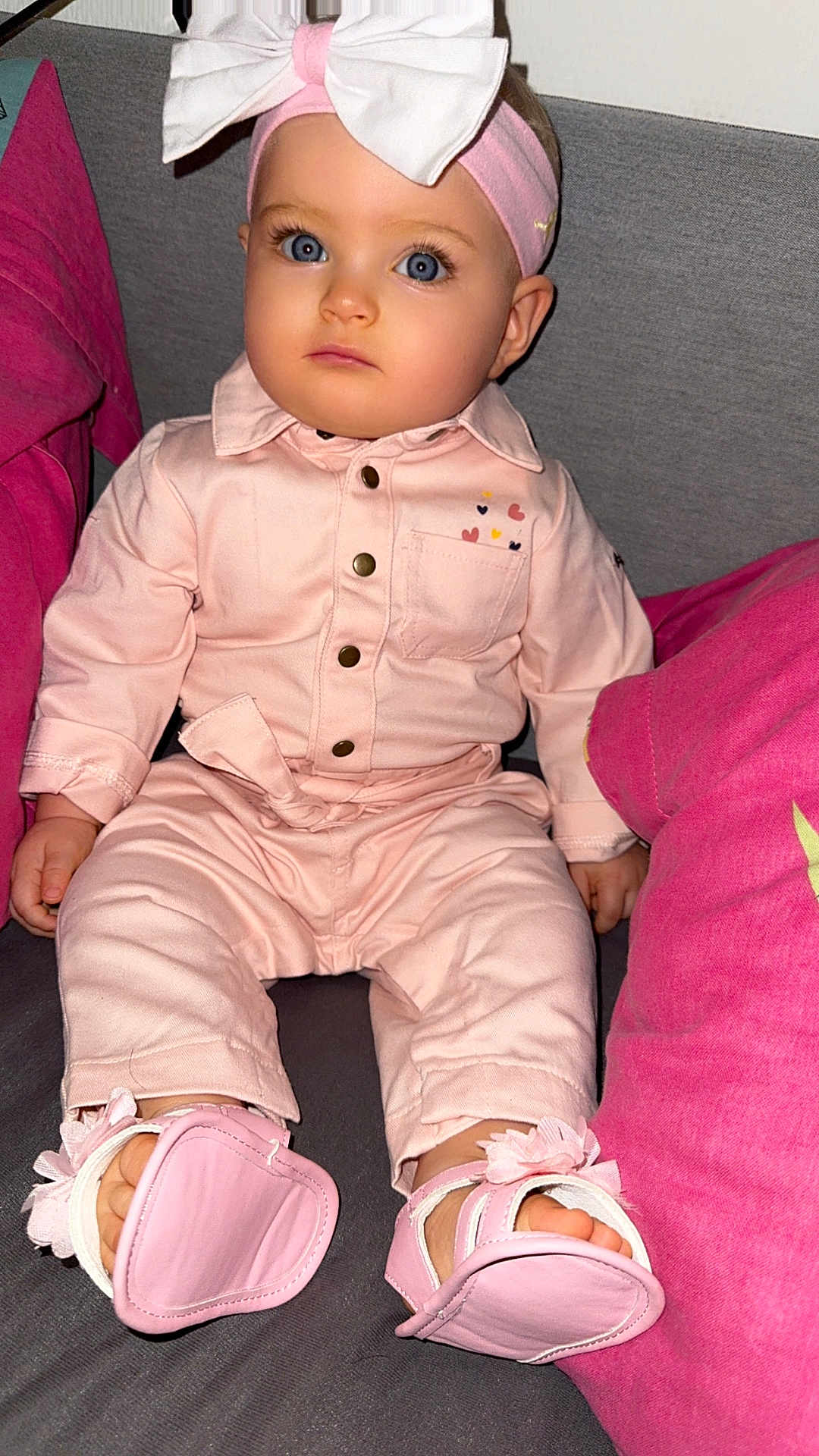 Angelina participe au concours pour gagner de l'argent avec cette photo : baby, child, pink_clothing, headband, bow, blue_eyes, sitting, couch, pillow, footwear, indoor, portrait, cute, infant, apparel, fashion, person, face, young_child, soft_lighting