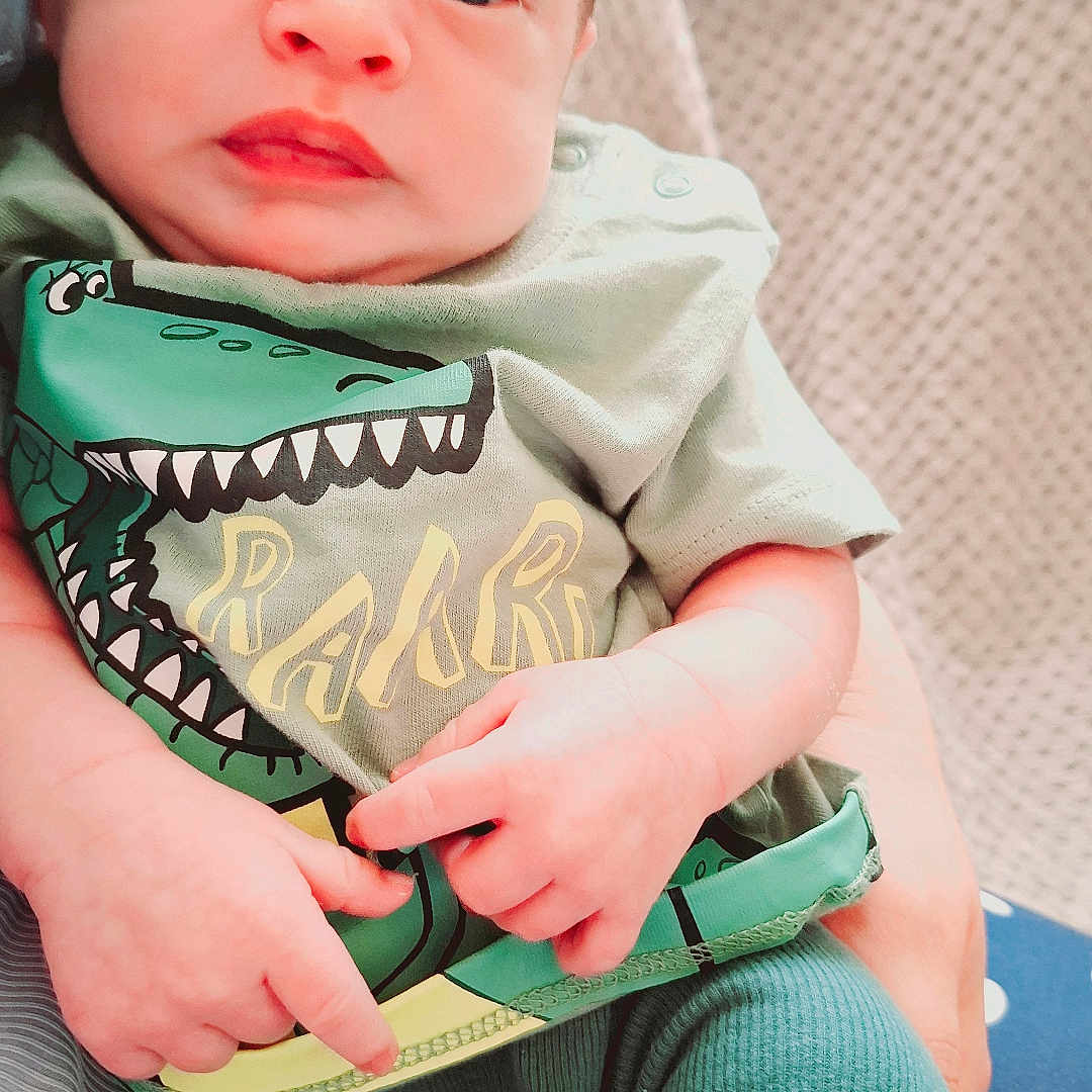 Louis is registered to the contest to win money with this photo: baby, blanket, casual, child, closeup, comfortable, cozy, cute, dinosaur_print, eyes, face, green_clothing, hands, indoor, infant, person, portrait, sitting, soft_texture, young