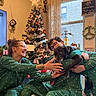 christmas_tree, dog, person, pajamas, glasses, indoor, window, decorations, gift, smile, rug, plant, candle_holder, tattoo, glass_window, holiday, tree_star, wreath, joy, home