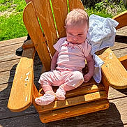 Zayley is registered to the contest to win money with this photo: baby, child, wooden_chair, pink_clothing, outdoor, sunlight, deck, towel, socks, grass, person, infant, summer, nature, wood, baby_clothes, serious_expression, seat, sunshine, barefoot