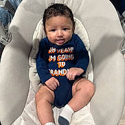 Alejando Noriega joined the competition — help win amazing prizes! baby, child, infant, onesie, tongue_out, baby_seat, cushion, toy, curly_hair, socks, playful, indoor, cute, smiling, person, young_child, comfortable, colorful_toy, text_on_clothing, relaxed