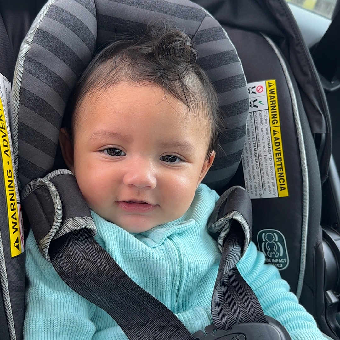 Alejando Noriega is registered to the contest to win money with this photo: baby, car_seat, child, closeup, curly_hair, cute, graco, indoors, infant, person, portrait, safety_harness, seatbelt, smile, straps, turquoise_clothing, vehicle, warning_label, window, young_child