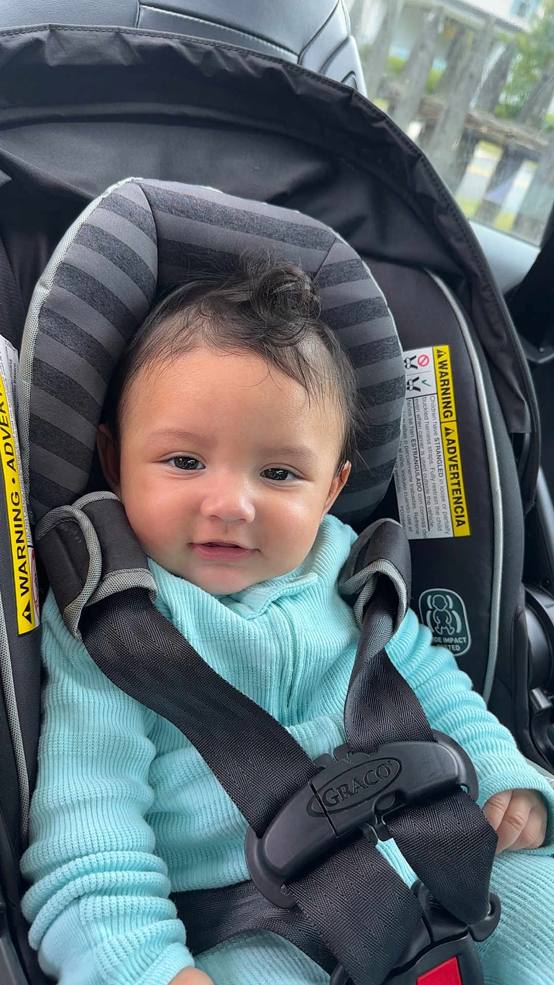 Alejando Noriega is registered to the contest to win money with this photo: baby, child, car_seat, graco, seatbelt, turquoise_clothing, curly_hair, smile, infant, safety_harness, portrait, indoors, vehicle, window, straps, warning_label, cute, young_child, person, closeup