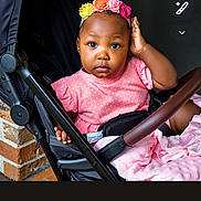 Brennayah joined the competition — help win amazing prizes! baby, baby_girl, brick_wall, casual, child, colorful, curious, cute, expression, flower_headband, girl, headwear, indoors, infant, person, pink_dress, portrait, seated, stroller, young_child
