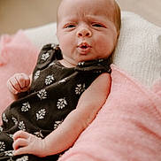 Addison joined the competition — help win amazing prizes! baby, infant, face, expression, black_dress, floral_pattern, blanket, pink_blanket, white_blanket, skin, hand, newborn, cute, portrait, indoors, soft_lighting, person, resting, young_child, cozy