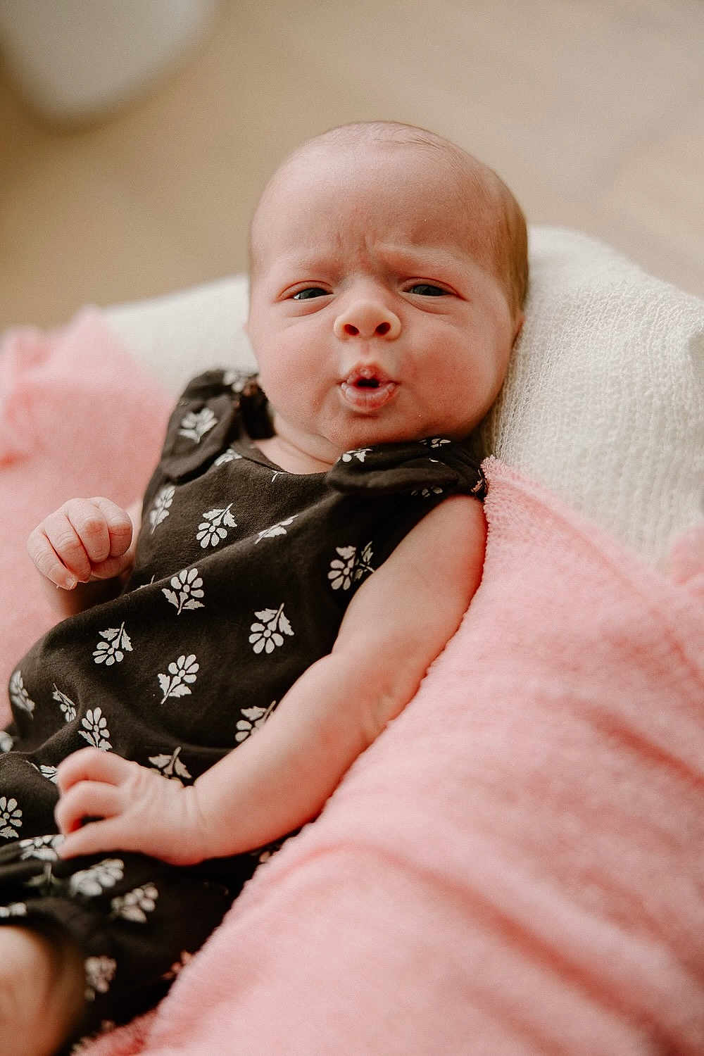 Addison joined the competition — help win amazing prizes! baby, infant, face, expression, black_dress, floral_pattern, blanket, pink_blanket, white_blanket, skin, hand, newborn, cute, portrait, indoors, soft_lighting, person, resting, young_child, cozy