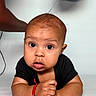 baby, infant, child, portrait, close_up, wide_eyes, sitting, black_shirt, drool, bracelet, red_thread, table, indoor, home, face, eyes, hands, arms, adult_arm, photography