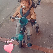 Arthur participe au concours pour gagner de l'argent avec cette photo : child, toddler, tricycle, pacifier, jacket, outdoor, sidewalk, brick_wall, toy, canopy, footwear, curious, calm, street, urban, casual, baby, transportation, play, winter_clothing