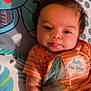 Zylus joined the competition — help win amazing prizes! baby, infant, child, cute, tongue_out, orange_shirt, striped_clothing, shark_graphic, playmat, colorful, patterned, lying_down, dark_hair, small_hands, closeup, indoors, soft_lighting, adorable, smiling, person