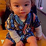 toddler, child, curly_hair, sitting, table, patterned_clothing, socks, indoor, cute, portrait, baby, hands, face, large_eyes, wooden_surface, love_hearts, colorful, casual_wear, expressionless, person