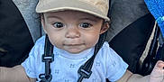 Zylus is registered to the contest to win money with this photo: baby, child, cap, stroller, seatbelt, clothing, shorts, white_shirt, curly_hair, outdoor, sunlight, face, hands, safety_harness, infant, cute, casual, expression, seat, summer