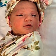 Mia is registered to the contest to win money with this photo: baby, newborn, infant, face, headband, floral, blanket, swaddle, sleepy, soft, skin, person, portrait, indoors, bed, cute, peaceful, closeup, child, head