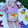 baby, infant, blanket, butterfly, hat, pink_bow, sunglasses, grass, outdoor, colorful, toy, foot, legs, pattern, flower, accessory, cute, soft_texture, playful, child