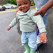 Khadarii joined the competition — help win amazing prizes! adult_hand, casual, child, cute, fashion, green_boots, jeans, outdoor, pavement, person, playful, rain_boots, rainy_day, smile, standing, street, support, sweater, toddler, wet_surface