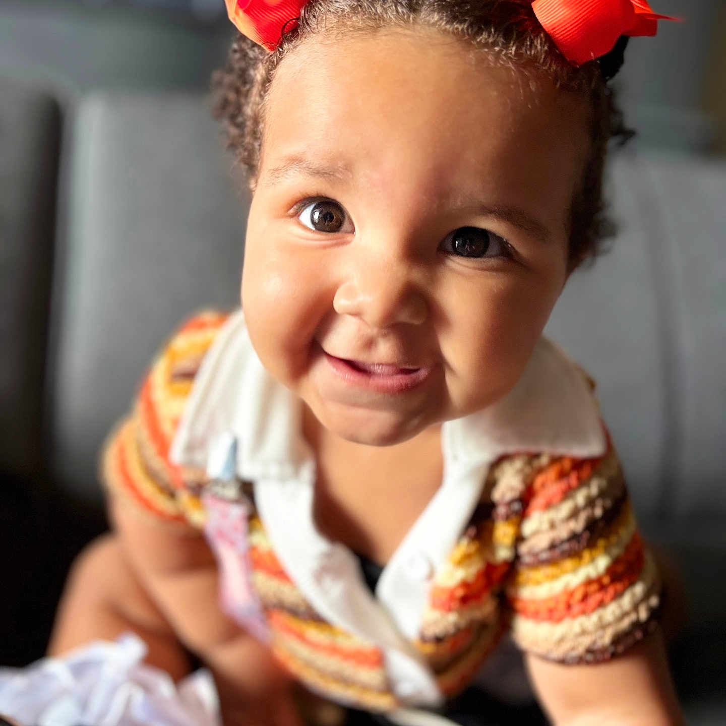 Yamiah is registered to the contest to win money with this photo: baby, child, close_up, colorful, curly_hair, cute, expression, eyewear, face, fashion, happy, indoors, knit_clothing, orange_bows, person, portrait, sitting, smiling, toddler, young
