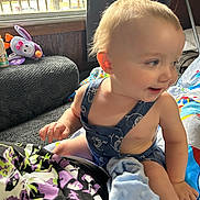 Kai joined the competition — help win amazing prizes! toddler, child, indoor, overalls, toy, blanket, couch, window, daylight, person, face, smile, curly_hair, colorful, playful, home, furniture, soft_toy, fabric, relaxed