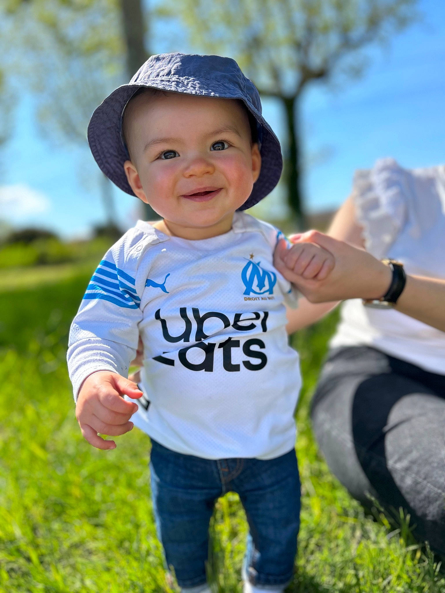 Kaëlan a rejoint le concours — aidez-le/la à gagner de superbes lots ! azure, clothing, facial_expression, flash_photography, gesture, grass, happy, headwear, jeans, joy, mammal, people_in_nature, person, plant, skin, sky, sleeve, smile, standing, toddler