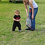 child, toddler, woman, grass, outdoor, boat, bag, egg, playing, curious, casual_clothing, jeans, tank_top, puma, spring, nature, activity, family, daytime, fun