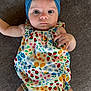 baby, infant, child, headband, blue_headband, floral_romper, flower_pattern, colorful_clothing, lying_down, brown_background, cute, wide_eyes, portrait, skin, hand, legs, baby_fashion, closeup, indoors, soft_light
