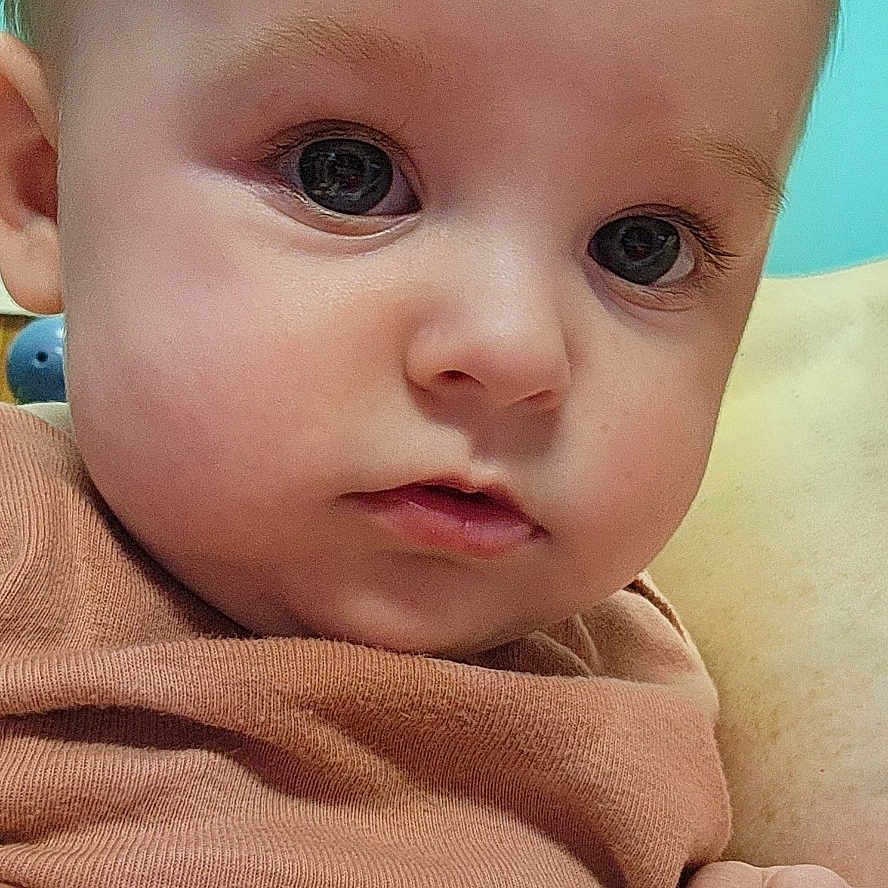 Raider is registered to the contest to win money with this photo: baby, babywear, child, closeup, clothing, cute, expression, eyes, face, hand, holding, human, indoor, infant, person, portrait, skin, skin_texture, soft, young