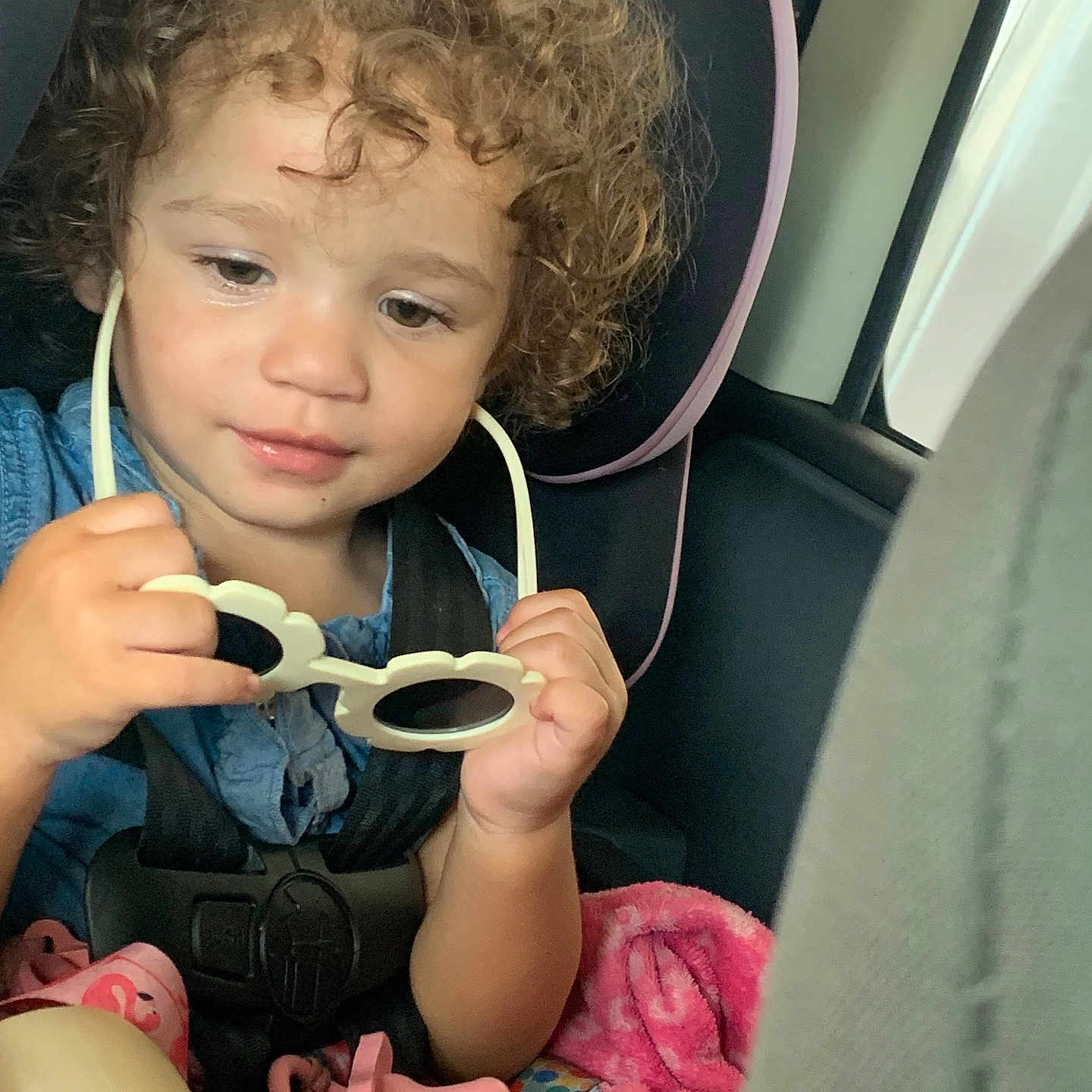 Myrakle is registered to the contest to win money with this photo: baby, blanket, blue_clothing, car_interior, car_seat, child, curly_hair, cute, focus, hands, indoor, infant, pacifier, pink, portrait, safety, seatbelt, sunglasses, toddler, vehicle