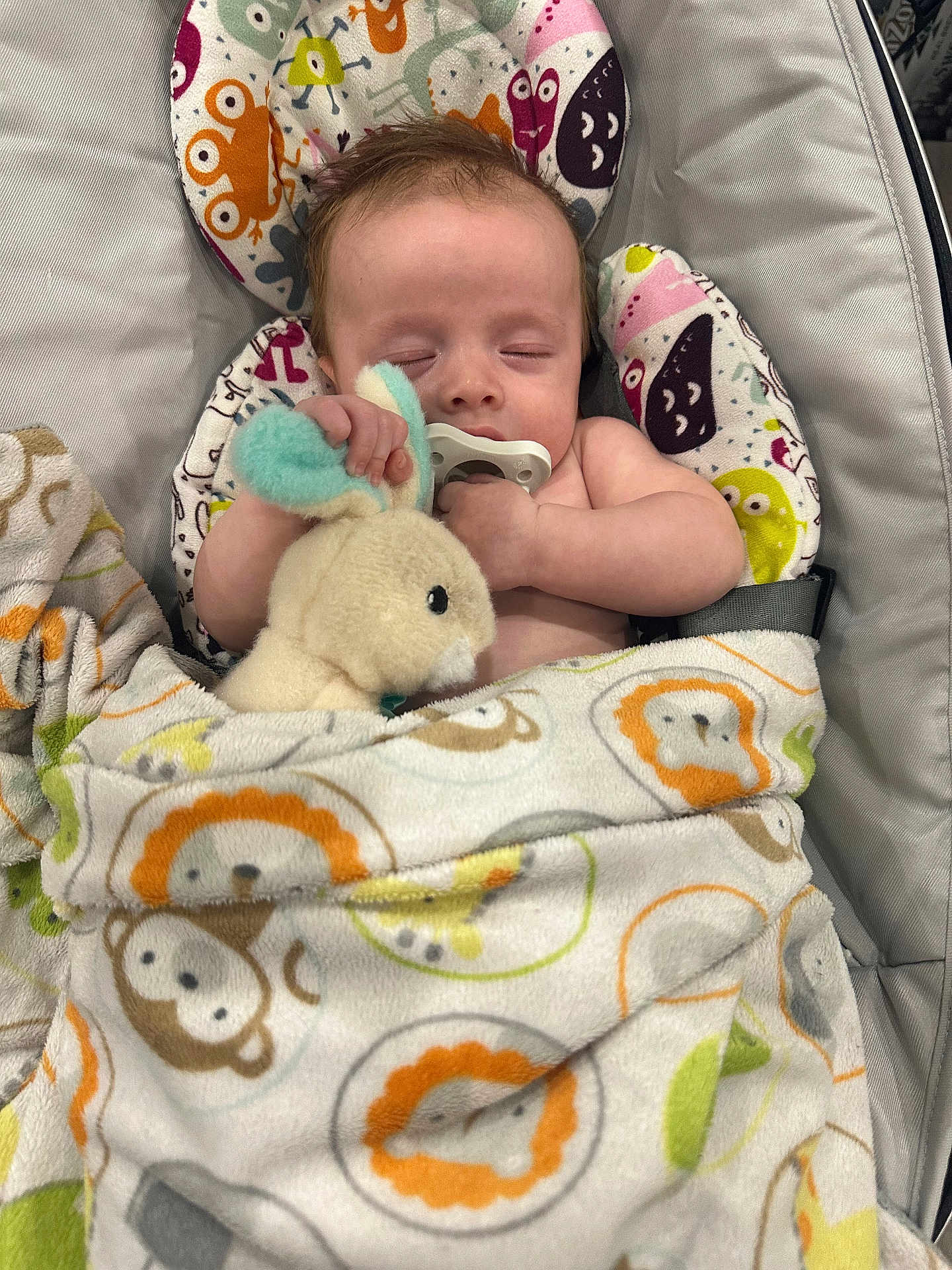 Kaysen is registered to the contest to win money with this photo: baby, infant, sleeping_baby, pacifier, plush_toy, stuffed_animal, blanket, animal_pattern, monkey_pattern, lion_pattern, baby_seat, hand, arm, face, portrait, indoors, close_up, cute, nap, soft_fabric