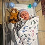 newborn, baby, hospital, bassinet, blanket, stuffed_animal, infant, wrapped, cute, expression, tongue_out, footprints, hat, medical, crib, girl, hospital_room, soft_toy, swaddled, lying_down