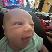 Adelyn is registered to the contest to win money with this photo: baby, closeup, smiling, indoor, clothing, onesie, face, person, video_game, television, living_room, furniture, lamp, door, blanket, happy, infant, human, child, casual