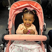 Lael is registered to the contest to win money with this photo: toddler, child, stroller, smiling, baby, toy, blanket, pink, hair_buns, cute, indoor, public_transport, people, clothing, happy, portrait, person, seat, transportation, urban