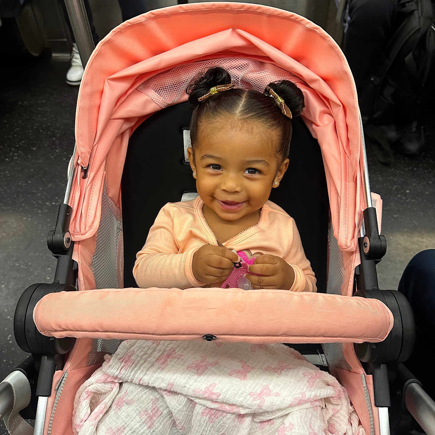 Lael is registered to the contest to win money with this photo: toddler, child, stroller, smiling, baby, toy, blanket, pink, hair_buns, cute, indoor, public_transport, people, clothing, happy, portrait, person, seat, transportation, urban