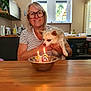 woman, dog, glasses, birthday, candles, kitchen, table, window, metal_bowl, celebration, indoor, smile, pet, light, number_candles, short_hair, striped_shirt, wooden_surface, happy, holding