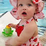 Esmae is registered to the contest to win money with this photo: baby, child, swimsuit, hat, strawberry_pattern, pool, water, toy, octopus_toy, curious, expression, summer, outdoor, playful, cute, skin, pink, red, childhood, fun