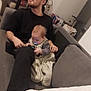 baby, blanket, bonding, casual, comfort, couch, curious, family, furniture, glasses, holding, home, indoor, living_room, man, pacifier, person, relaxed, seated