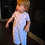 acoustic_foam, barefoot, blond_hair, casual_clothing, child, curious, dark_background, expression, floor, indoor, indoors, looking_away, person, portrait, short_sleeves, soft_lighting, standing, toddler, white_overalls, young_child