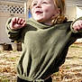 casual_clothing, cheerful, child, daylight, face, fence, fun, grass, green_sweater, happy, nature, outdoor, person, playful_pose, potted_plants, smile, sunlight, tree_shadow, yard, young