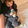 Axell is registered to the contest to win money with this photo: child, toddler, boy, sitting, bed, blanket, bottle, drinking, straw, clothing, hoodie, pants, shoes, indoors, bedroom, portrait, cozy, brown_hair, face, candid