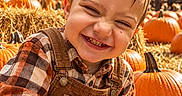 Axell is registered to the contest to win money with this photo: child, boy, smiling, outdoor, autumn, fall, pumpkin, pumpkin_patch, hay, corn_stalks, farm, harvest, overalls, plaid_shirt, portrait, closeup, happy, nature, daylight, seasonal
