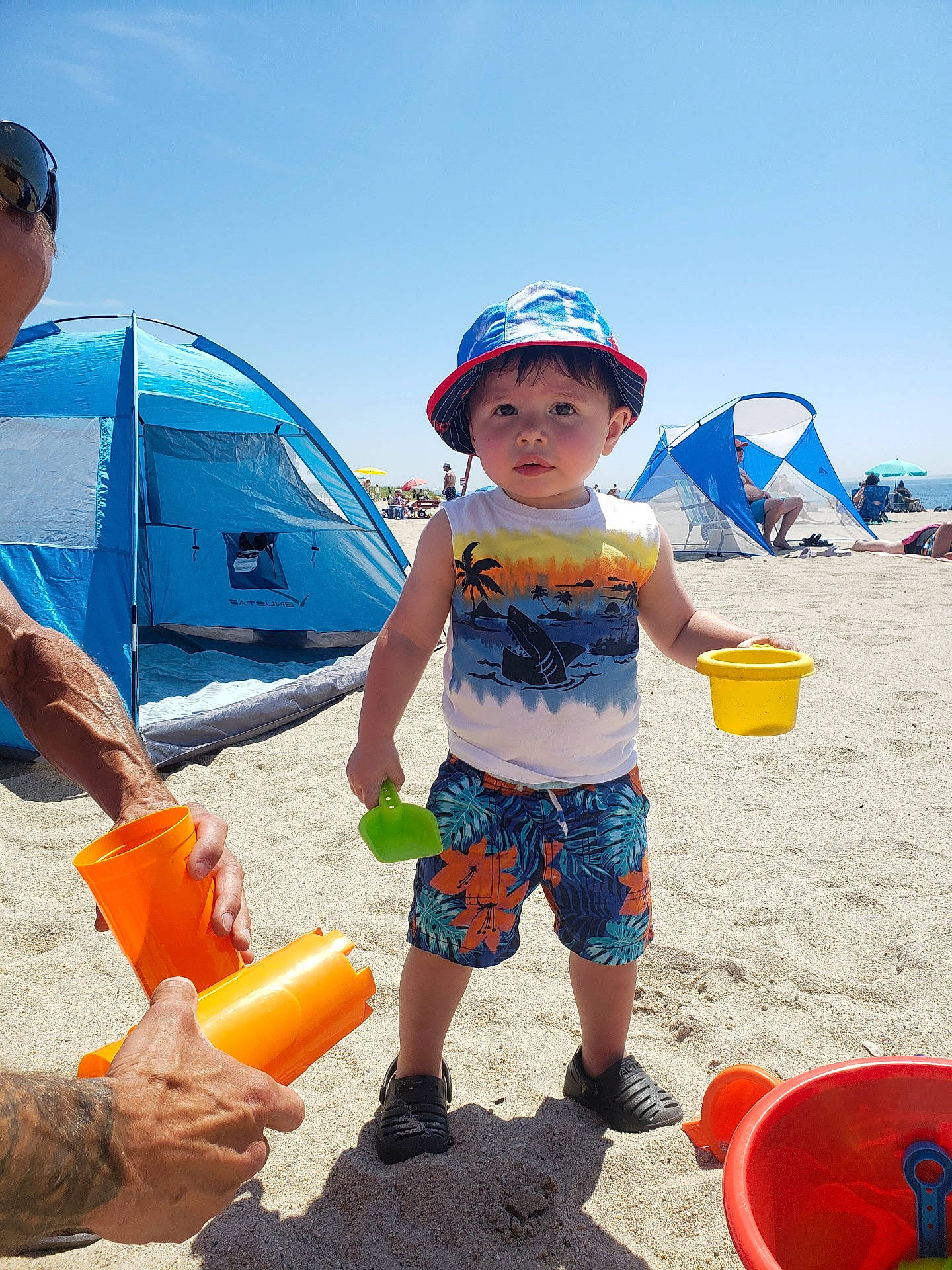 Jayce is registered to the contest to win money with this photo: beach, blue, body_of_water, child, electric_blue, fun, headwear, landscape, leisure, natural_environment, people_in_nature, person, personal_protective_equipment, play, recreation, sand, shade, shorts, sky, toddler