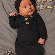 Amelia is registered to the contest to win money with this photo: baby, infant, black_outfit, headwrap, blanket, milestone_sign, name_text, portrait, newborn, cute, lying_down, soft_texture, one_month, child, small_hands, button_detail, face, expression, sleepwear, cozy