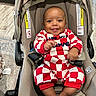 baby, smiling, child, stroller, onesie, red_and_white, checkered, happy, infant, seat, indoor, footwear, barefoot, clothing, person, cute, young_child, car_seat, baby_girl, cheerful